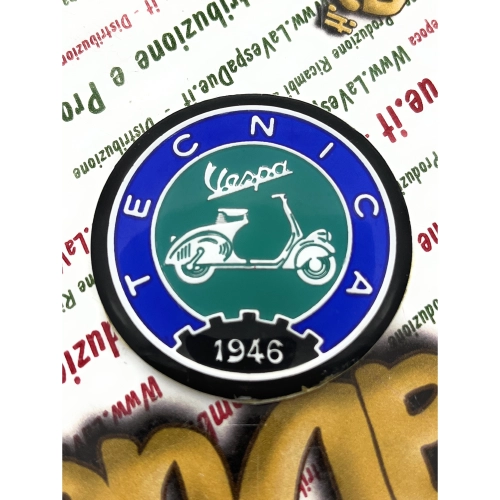 Écusson en résine de 53 mm de diamètre sur base en aluminium. Logo vintage VESPA TECNICA 1946 en aluminium bleu et vert, à appliquer sur les accessoires VESPA à l'aide d'un adhésif. Ø 53 mm