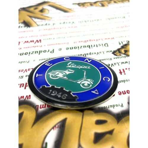 Écusson en résine de 53 mm de diamètre sur base en aluminium. Logo vintage VESPA TECNICA 1946 en aluminium bleu et vert, à appliquer sur les accessoires VESPA à l'aide d'un adhésif. Ø 53 mm