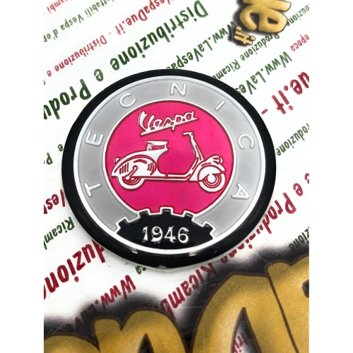Écusson en résine Ø 53 mm sur base en aluminium. Logo vintage VESPA TECNICA 1946, gris et rose, à appliquer sur les accessoires VESPA à l'aide d'un adhésif. Ø 53 mm