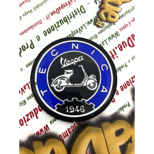 Écusson en résine de 53 mm de diamètre sur base en aluminium. Logo vintage VESPA TECNICA 1946 en aluminium bleu et noir, à appliquer sur les accessoires VESPA à l'aide d'un adhésif. Ø 53 mm