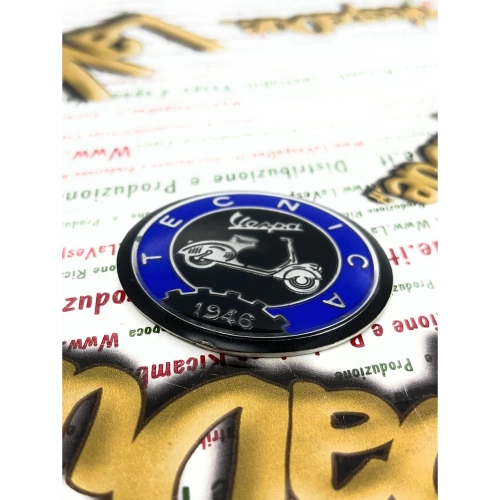 Écusson en résine de 53 mm de diamètre sur base en aluminium. Logo vintage VESPA TECNICA 1946 en aluminium bleu et noir, à appliquer sur les accessoires VESPA à l'aide d'un adhésif. Ø 53 mm